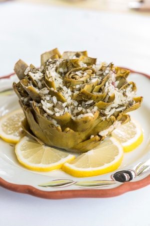 Baked artichoke with rice and lemons on white plateの写真素材