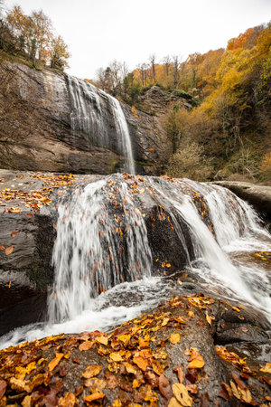 Autumn waterfall in the forest. Beautiful autumn landscape with falling leavesの写真素材