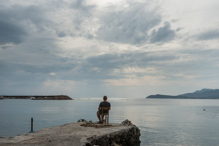 Man sitting on the pier and looking at the sea on a cloudy dayの写真素材