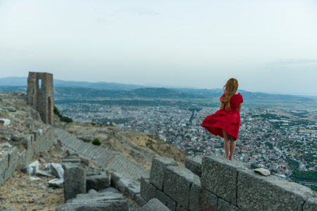 A girl in a red dress stands on the edge of the fortress and looks at the city.の写真素材