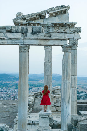 A young girl in a red dress is standing on the ruins of the ancient city.の写真素材