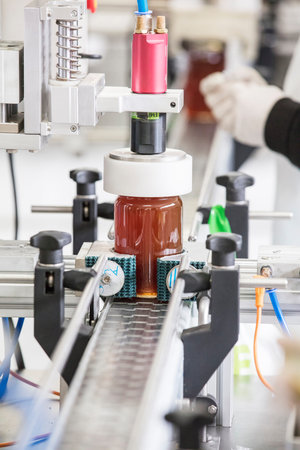 Filling empty jars with fresh honey in factory.