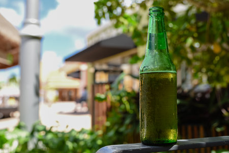 A green bottle of beer is sitting on a railing. The bottle is half full and has condensation on the outside close upの写真素材