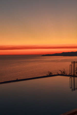 Sunset over sea with reflection from water in the swimming infinity pool at the evening. Relax at the end of the day. Colorful view.の写真素材