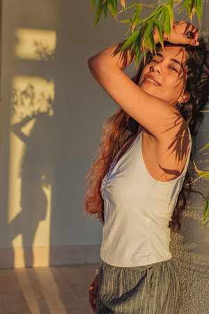 Portrait of young woman in shadows of leaves at sunny day, shadows on the wall, fashion view
