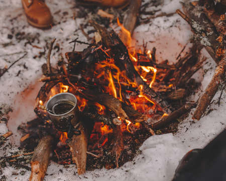 Iron mug on bonfire in snow at camping place in forestの写真素材