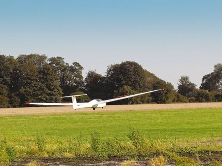 a glider landing near a field with trees and a blue skyの写真素材