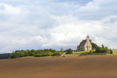 english landscape with a view across cultivated fields to an ancient church on a hill with trees and cloudy skyの写真素材