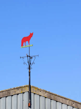 a weather vane in the shape of a fox on a farm building under a blue skyの写真素材