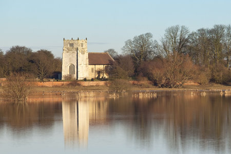 an english winter landscape with flooded fields trees and an ancient stone church under a blue sky