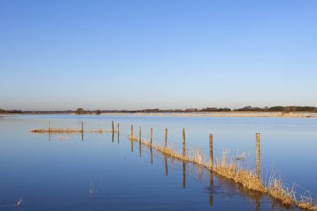 a line of fence posts submerged by flood water in winter under a blue skyの写真素材