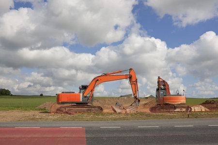 two big orange diggers by a roadside near agricultural fields under a dramatic cloudy sky