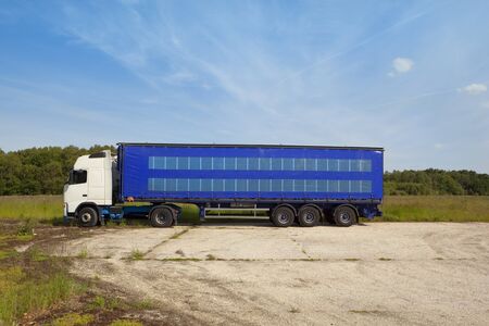 an articulated lorry with white cab and blue curtain sided trailer parked in a rural sitting with trees and a blue sky background and lots of copyspaceの写真素材