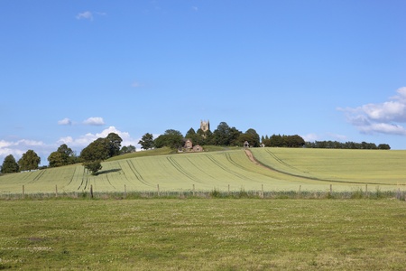 an english landscape with a view across fields of clover and wheat to a hilltop church under a blue skyの写真素材