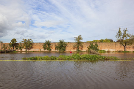 a walled garden submerged under flood water in autumn with trees and red tractor under a blue cloudy skyの写真素材