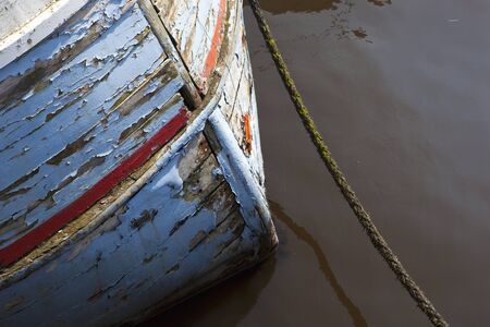 bow of an old wooden clinker built fishing boat with flaking paint and mooring ropeの写真素材