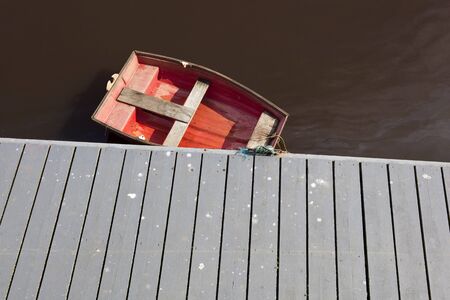 Small red boat moored to a wooden jettyの写真素材