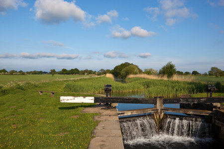 water pouring through canal lock gates beside a canal towpath with benches and picnic area in an agricultural landscapeの写真素材