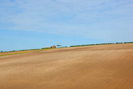 a derelict farm on a hillside surrounded by cultivated undulating fields with hedgerows under a blue sky in springtime in the yorkshire woldsの写真素材