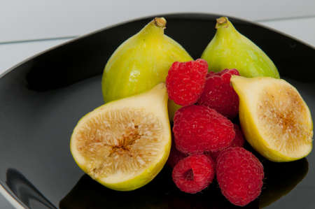 green figs and raspberries on black plateの写真素材