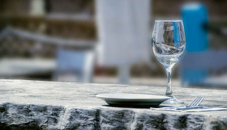 Wine glass, a plate and a fork on a wooden table in a cafe on the beachの写真素材