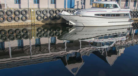 Reflection of the white yacht and berth buildings in the water of the Norwegian fjordの写真素材