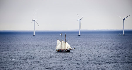 A sailboat in the sea against a background of wind power plants