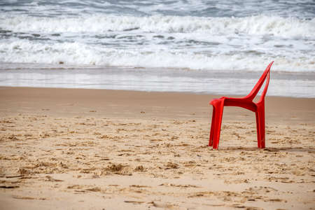 Red beach plastic chair on the sand close to the waterの写真素材