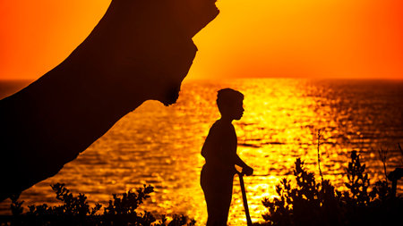 Silhouette of a boy on a scooter on the background of the sea at sunset