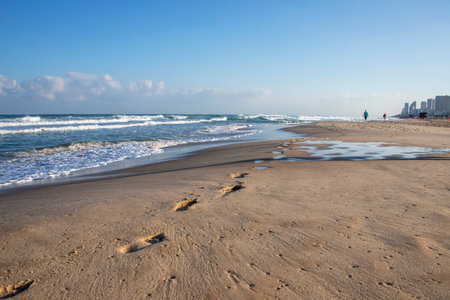 Footprints on the sand of a Mediterranean beach. Foamy waves and buildings on the horizon. Israelの写真素材