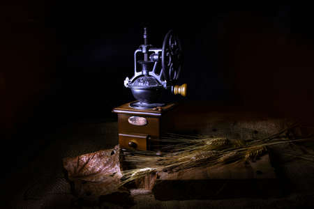 Stylized vintage coffee grinder, dry leaves and ears of wheat on a burlap-covered wooden table.の写真素材