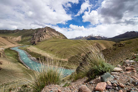 View of the river flowing between green hills with grass and stones in the foreground Kyrgyzstan. Tien Shanの写真素材
