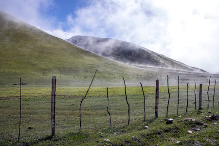 Agricultural fence. Green hills with descending fog. Kyrgyzstanの写真素材