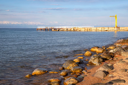 Side view of a pier on Issyk-Kul Lake with a mountain range with snowy peaks on the horizon against...