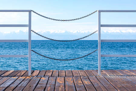 View of Issyk-Kul Lake and mountains with snow-capped peaks through the fence of a wooden pier. Kyrgyzstanの写真素材