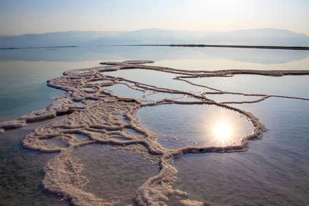 Reflection of the sun at dawn in the water of the Dead Sea with salt formations. Israelの写真素材