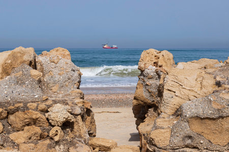 View of the Mediterranean Sea and the ship through the shell rock formations on the shoreの写真素材