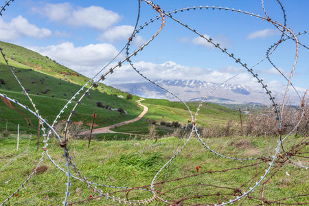 View of Mount Hermon with a snow-capped peak in the clouds through barbed wireの写真素材