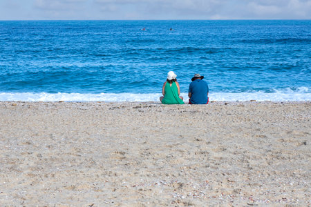 Couple man and woman sitting next to the water on the sandy beach on the mediterranean coastの写真素材