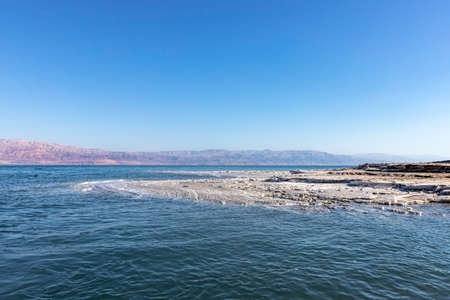 View of the mountains across the waters of the Dead Sea from the shore covered with salt formations.の写真素材