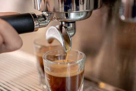 Gray coffee machine with two small glass cups filled with coffee on a metal grid in close up concept.の写真素材