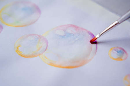 Female hand coloring bubble drawing with colored watercolors in a sketchbook on a white table.の写真素材