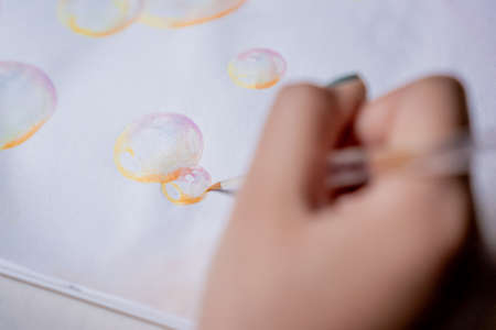 Female hand coloring bubble drawing with colored watercolors in a sketchbook on a white table.の写真素材