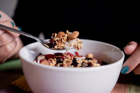 Person eating exquisite homemade oatmeal with banana, strawberries, granola, blueberry, coconut and...
