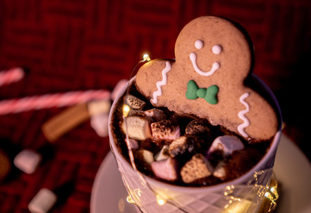 Exquisite cup of hot chocolate inside a white cup with a smiling gingerbread man cookie dipped with...
