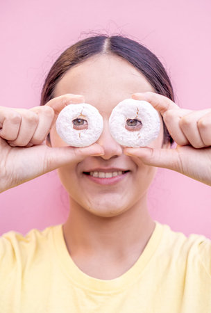 Latin woman holding two delicious donuts sprinkled with sugar glass in front of her eyes with a pink...
