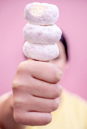 Exquisite donuts sprinkled with powdered sugar fitted on the thumb of a hand with a person on the back on a pink background.の写真素材