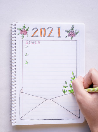 Hand writing in notebook to write New Year's resolutions on a table with a white tablecloth in close...