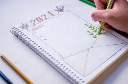 Hand writing in notebook to write New Year's resolutions on a table with a white tablecloth in close...