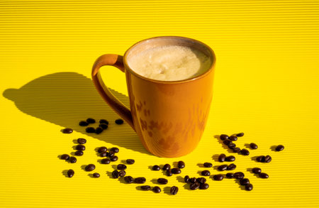 Exquisite freshly made sparkling coffee inside a brown cup with coffee beans scattered on a yellow table with a yellow background reflecting a black shadow on the side.の写真素材